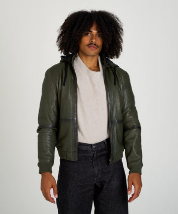 Cazadora bomber de piel verde oliva con capucha, cierre de cremallera y puños elásticos, estilo moderno y urbano.