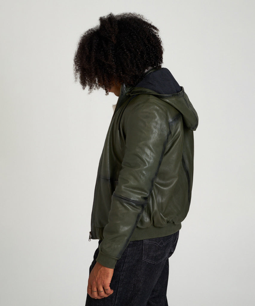 Cazadora bomber de piel verde oliva con capucha, cierre de cremallera y puños elásticos, estilo moderno y urbano.