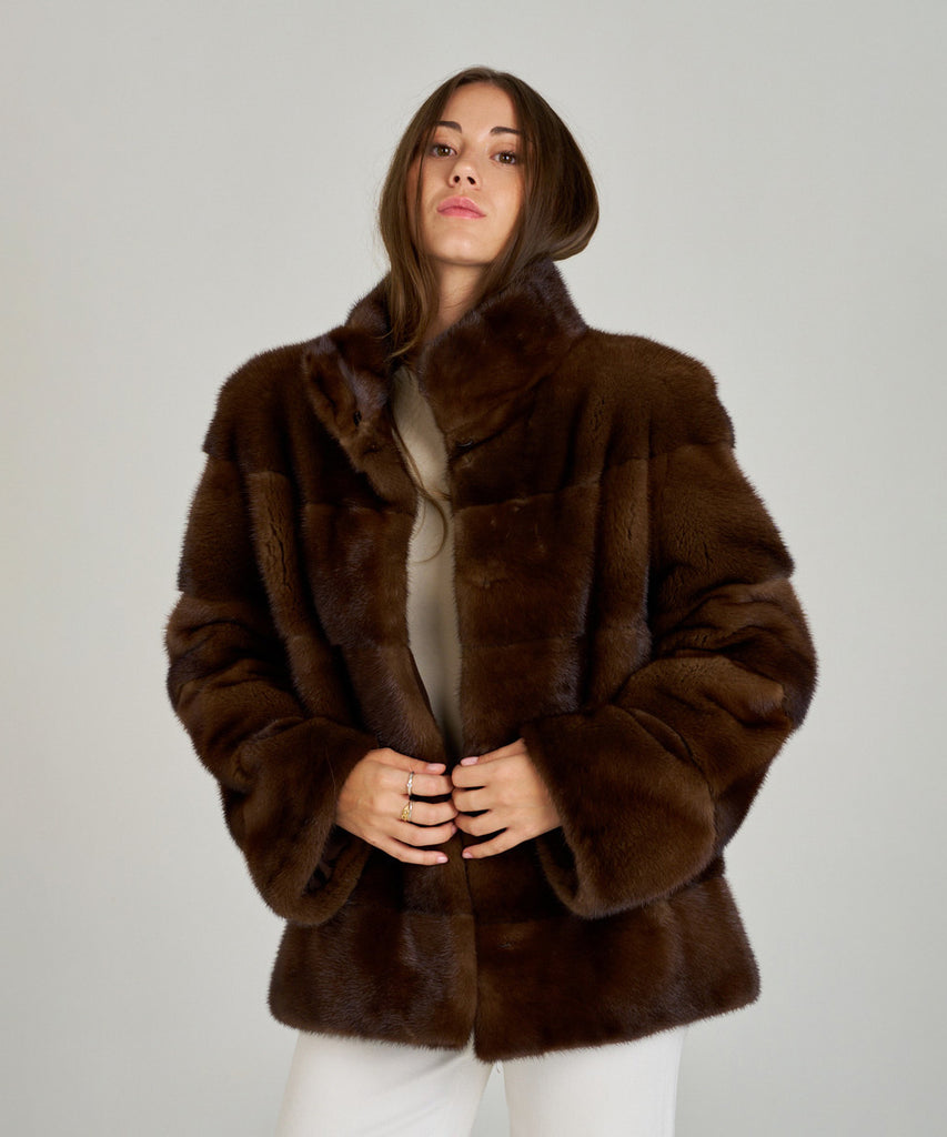 Cazadora de visón en color marrón, cuello envolvente y cierre oculto. Piel natural, corte recto y ligereza excepcional. Elegante, cálida y atemporal.