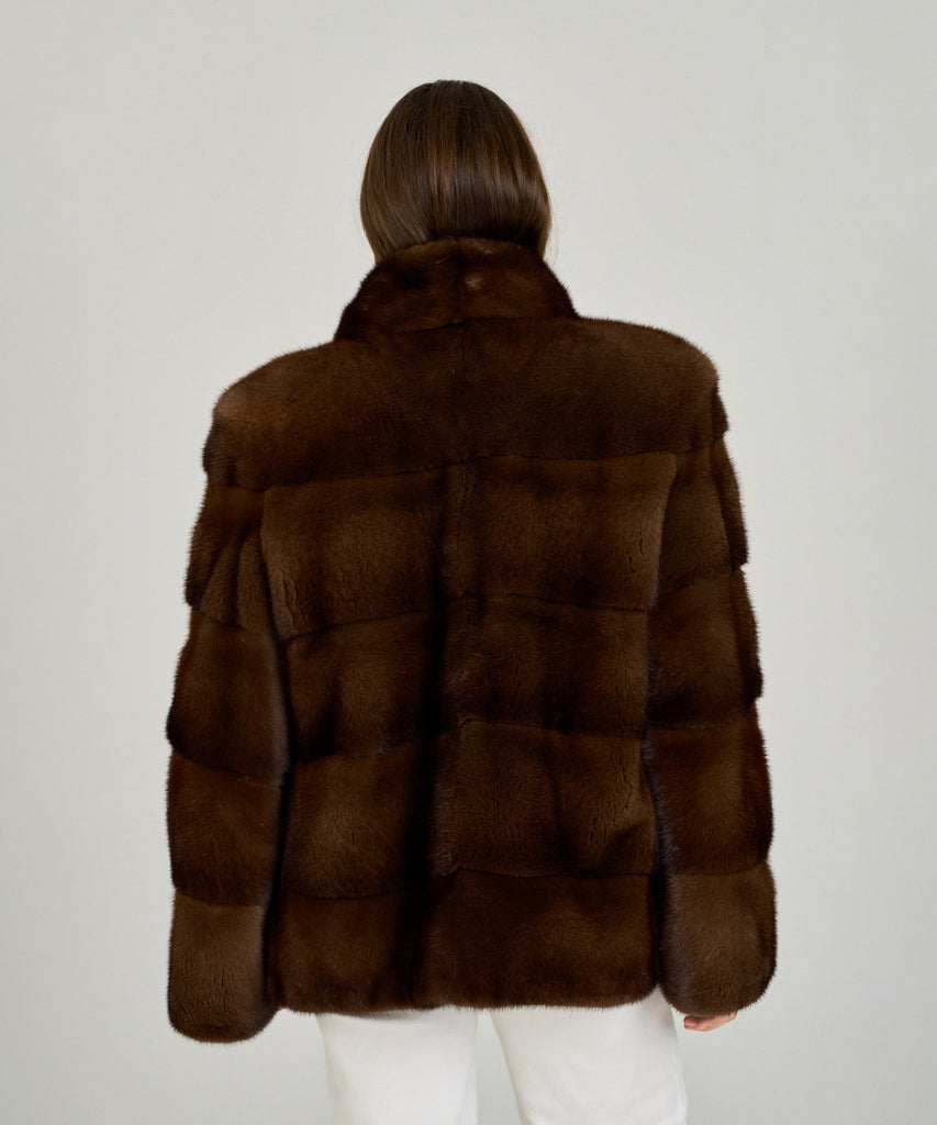 Cazadora de visón en color marrón, cuello envolvente y cierre oculto. Piel natural, corte recto y ligereza excepcional. Elegante, cálida y atemporal.